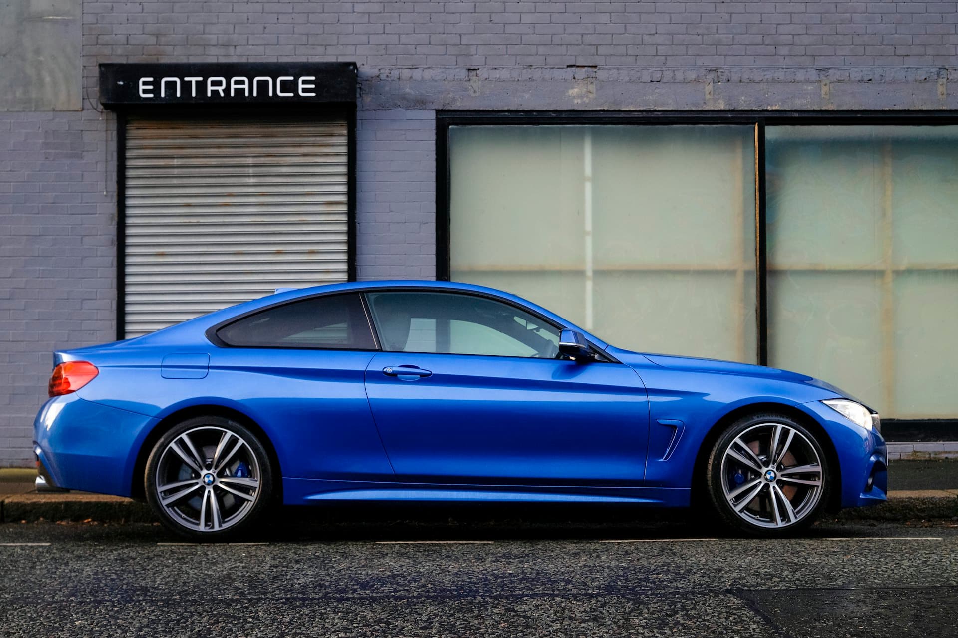A coupe wrapped in gloss blue, side profile against a city wall.