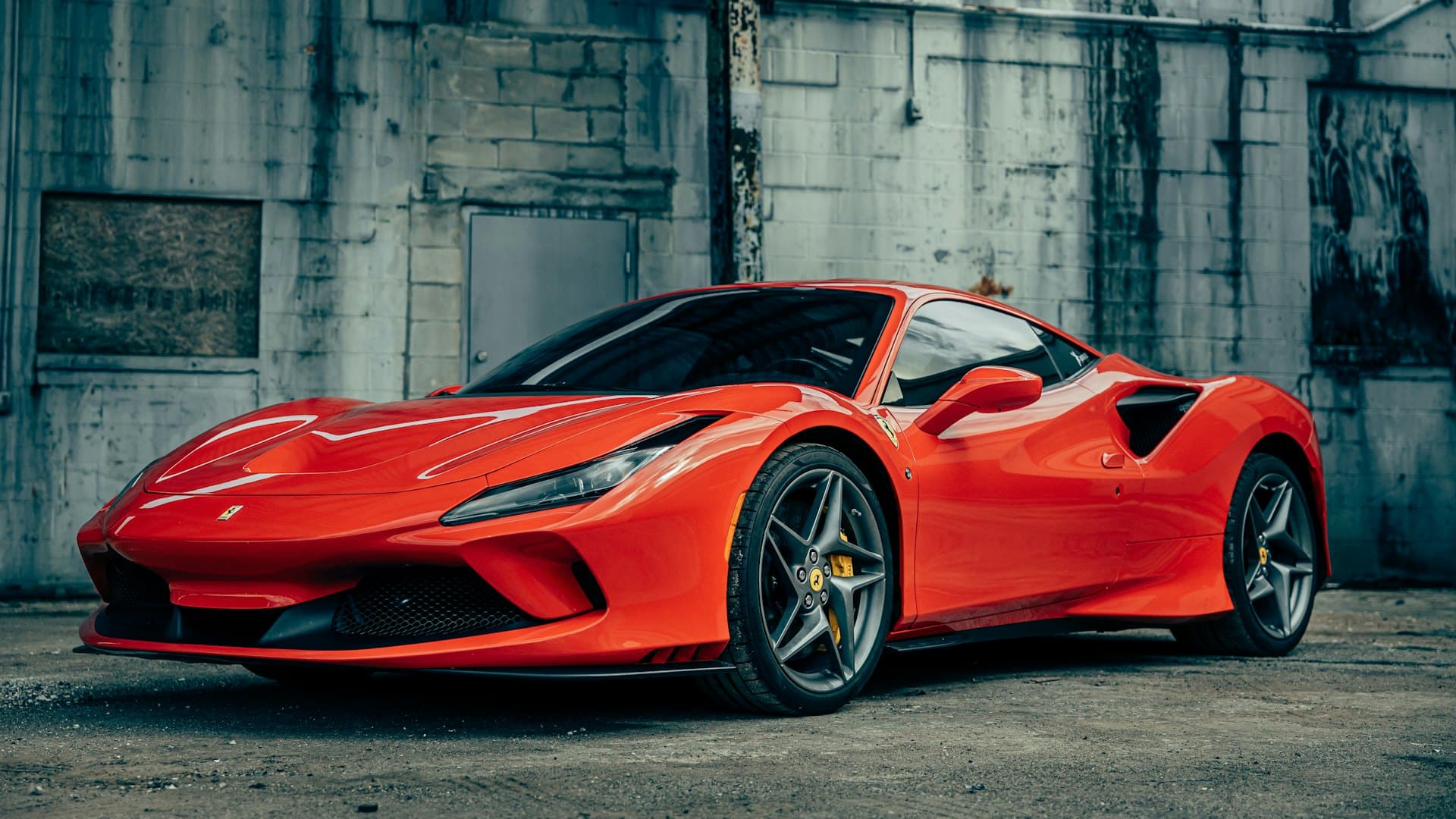 A supercar wrapped in gloss red against a raw industrial wall.